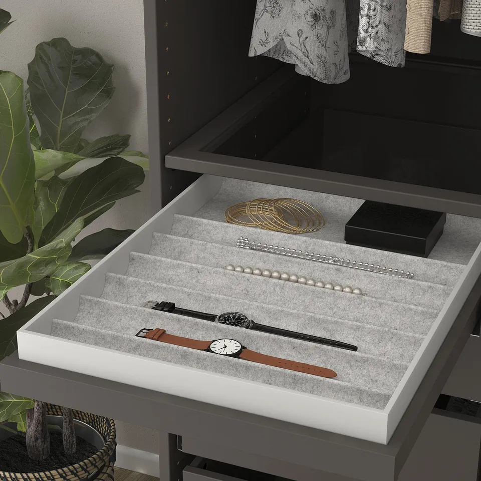 Open jewellery tray with watches, pearls, & bracelets in sections, beside a plant.