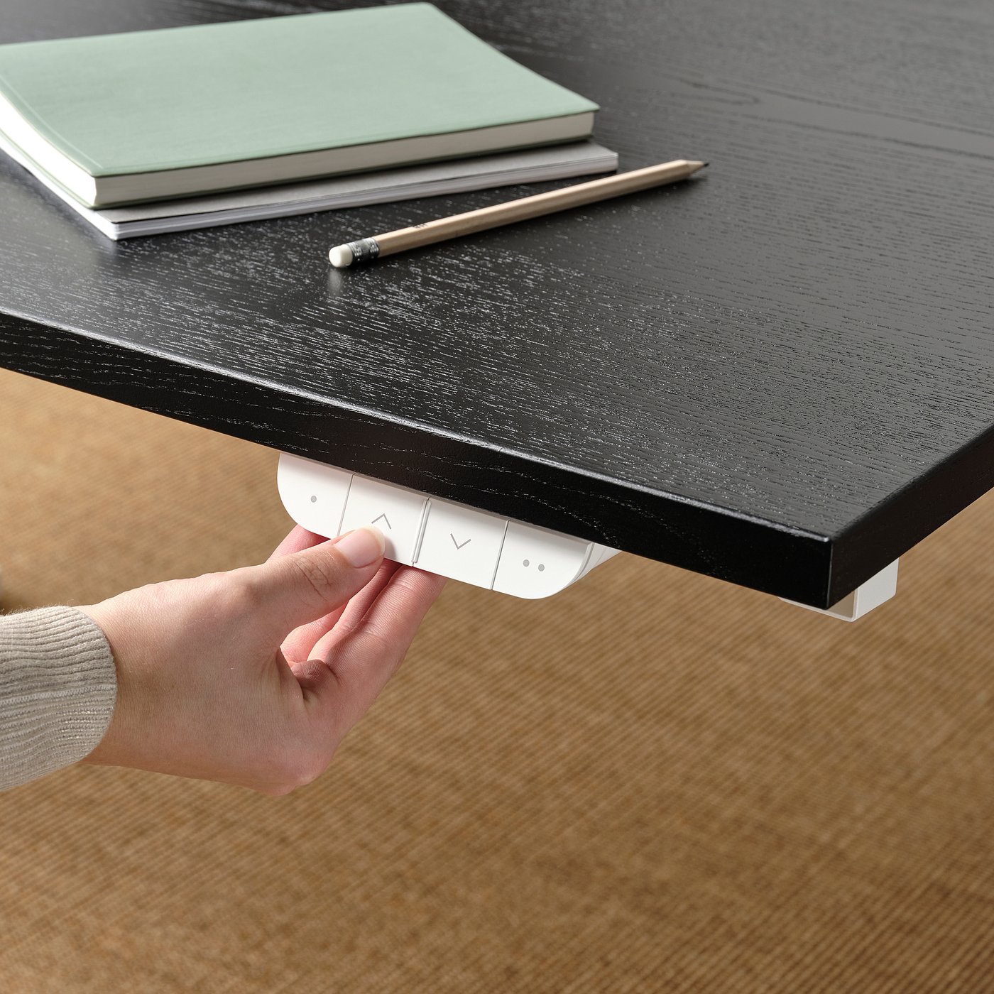 Hand presses button on electric desk controller, adjusting height for sit/stand.