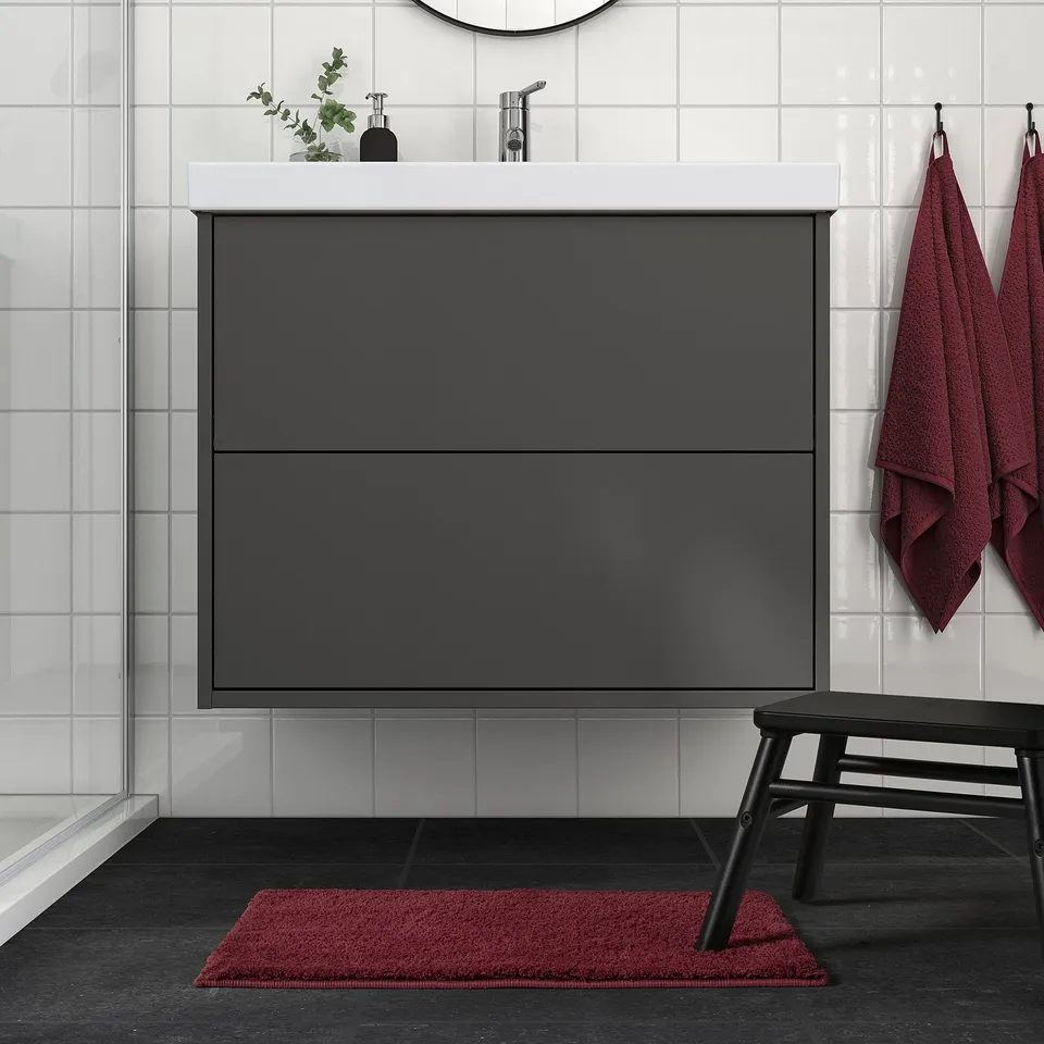 Modern bathroom with BACKMÅRA mat, dark grey, rectangular, under sink, matching red towels and bench.