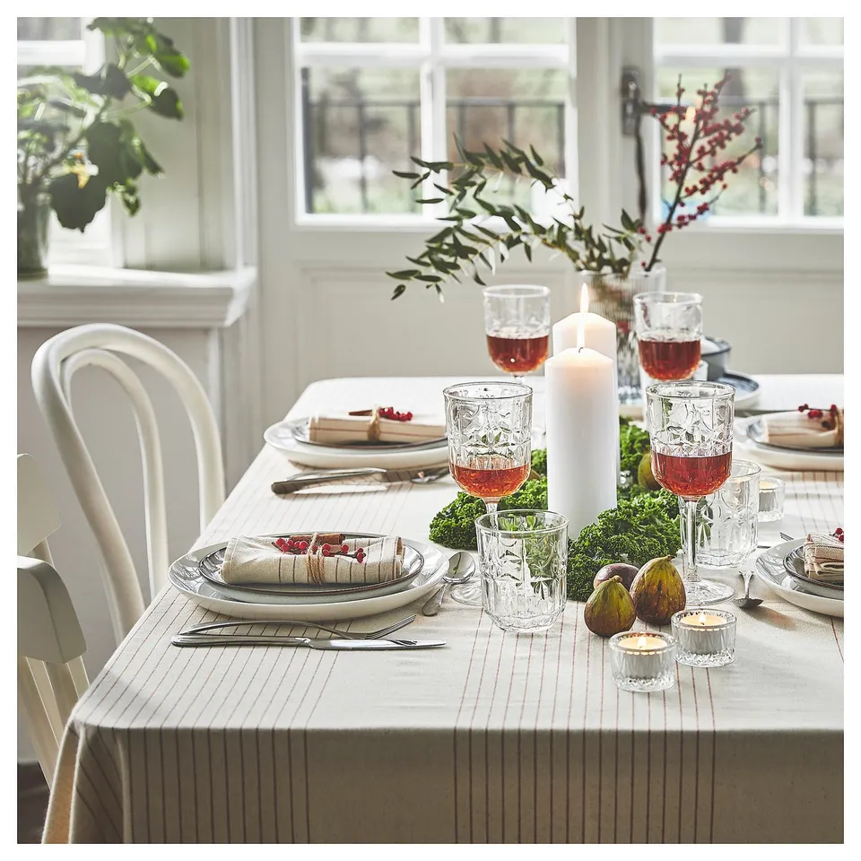 Table set with striped cloth, dinnerware, candles, fruit, greenery, soft lighting.
