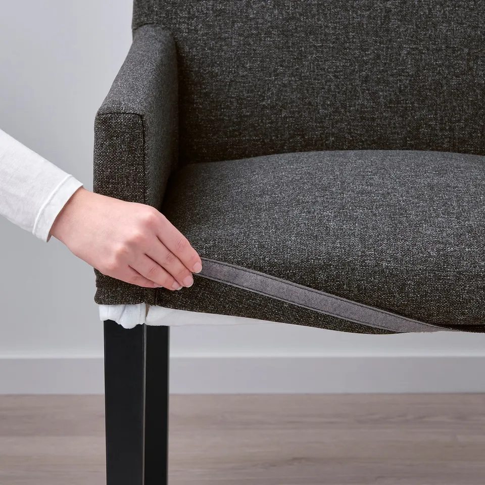 Image shows a person sliding the removable cover off a grey MÖRBYLÅNGA chair, demonstrating its easy-to-clean design.