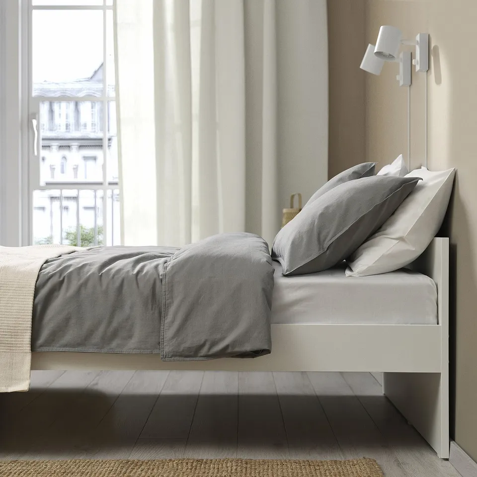 Modern bed with grey bedding, city view. Clean lines, minimalist, versatile.