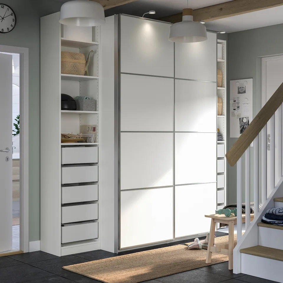 Modern white wardrobe with sliding doors, drawers, and shelves. Light wooden staircase nearby. Centred on clean, organised storage.