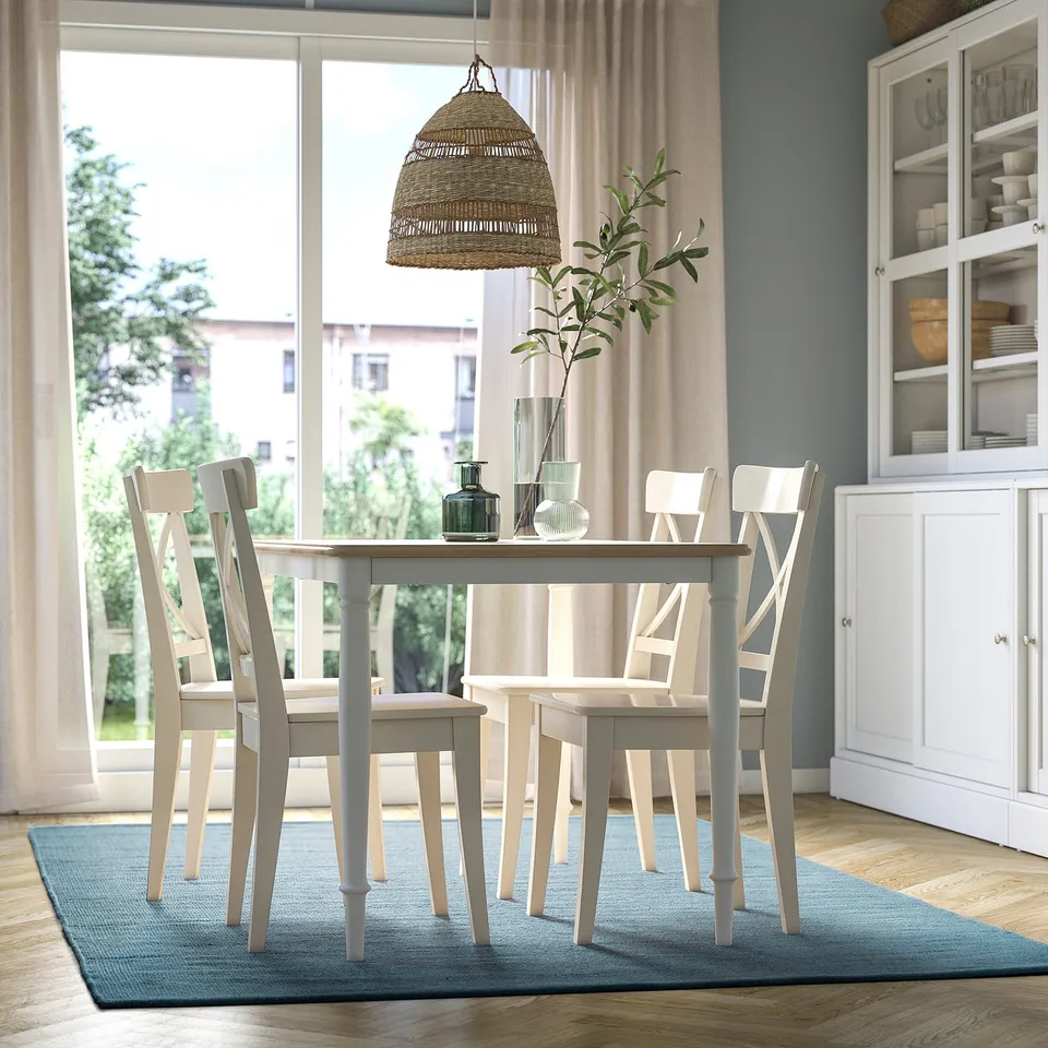 Bright dining area with light blue rectangle rug, white wooden dining set, and wicker pendant light.