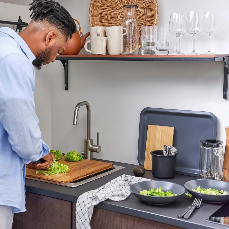 Person chopping lettuce on oak NORRSJÖN board over sink in modern kitchen with appliances.