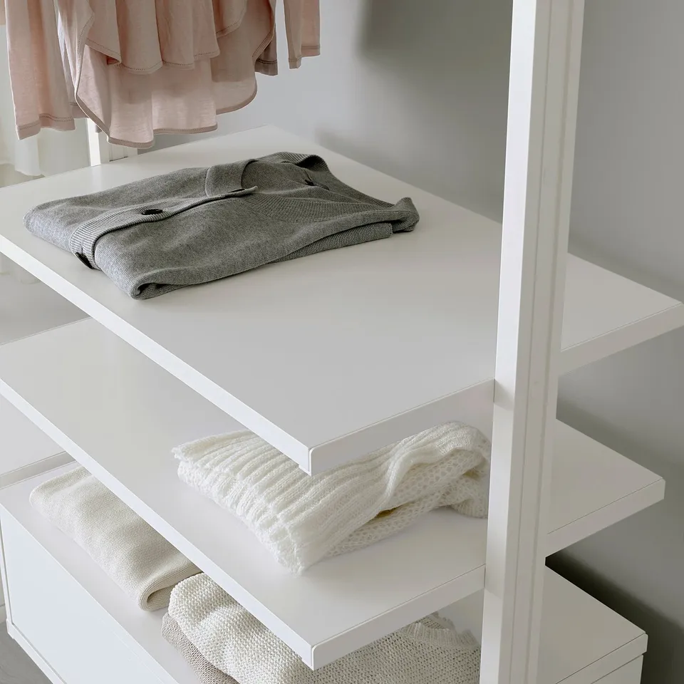 White closet with adjustable shelves, holding neatly folded grey sweater and cream-colored sweaters.