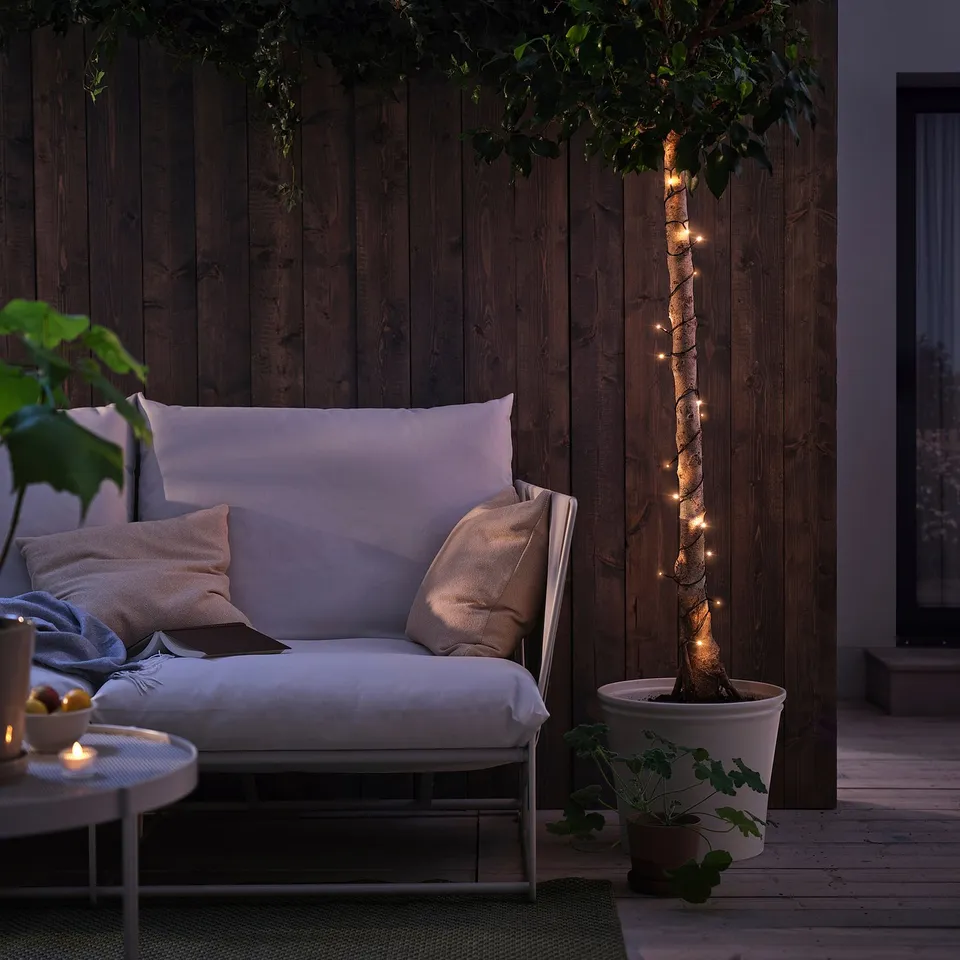Outdoor space with lighted tree, white sofa, and table. Decorated with GETKÅL string lights.