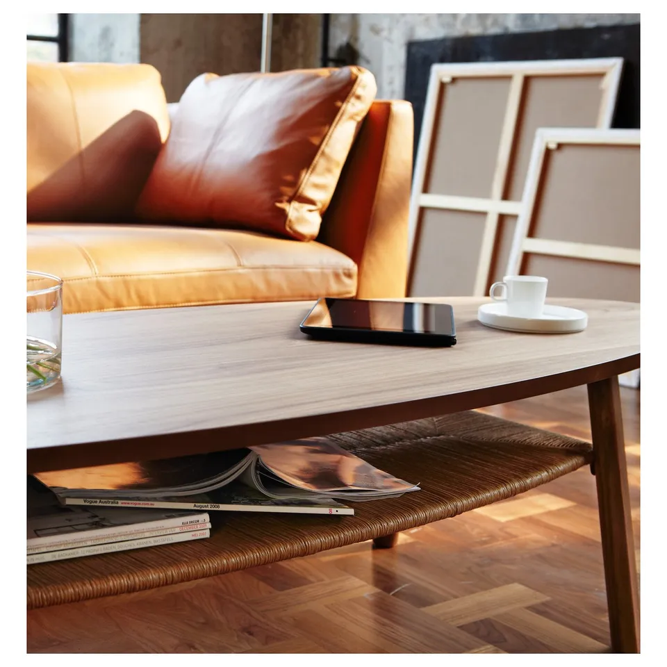 Modern living room with oval coffee table displaying walnut top and wood grain. Smartphone, mug, and magazines highlight its elegant design.