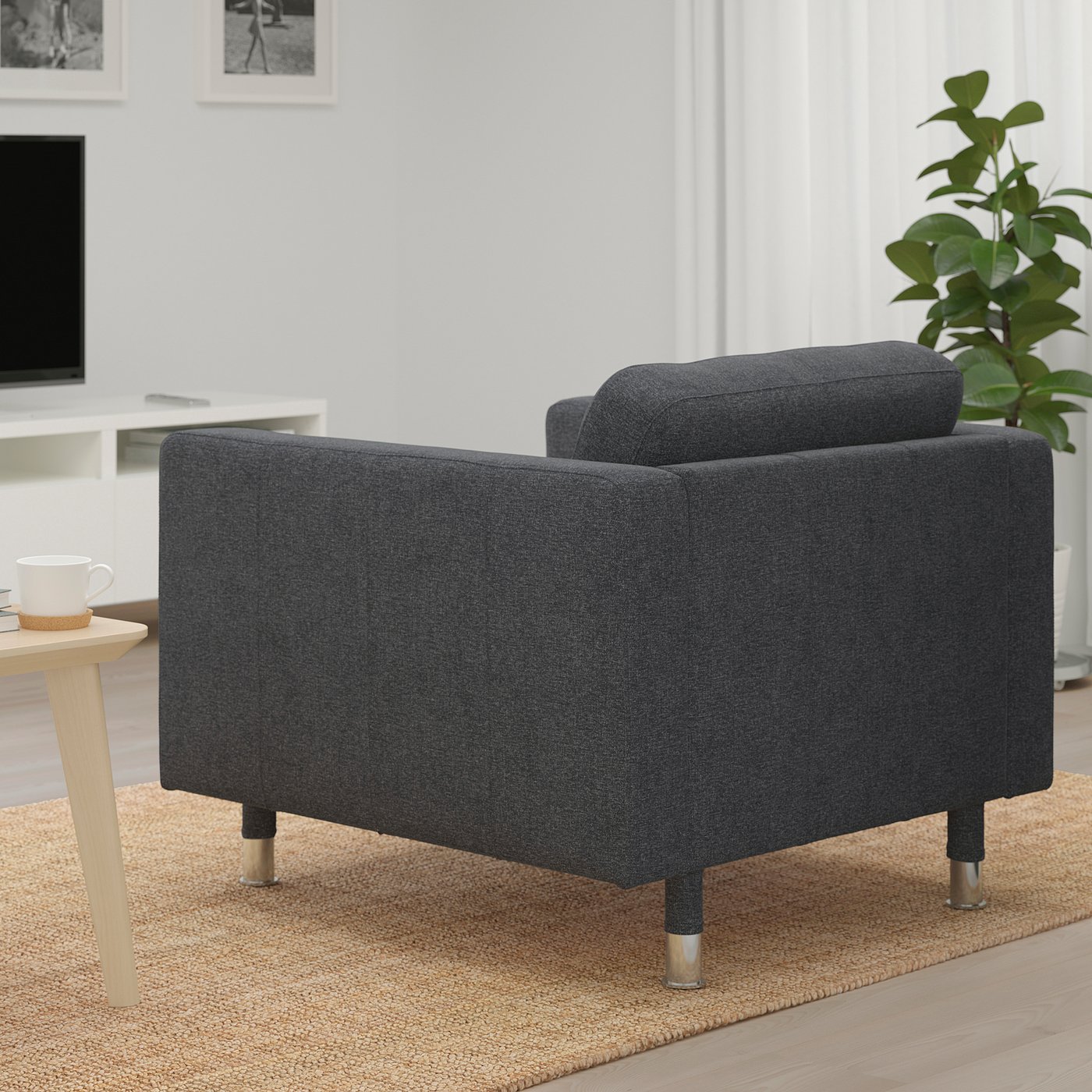 Dark grey modern armchair with wooden legs on a woven rug near a wooden side table with a coffee cup in a cosy living space.