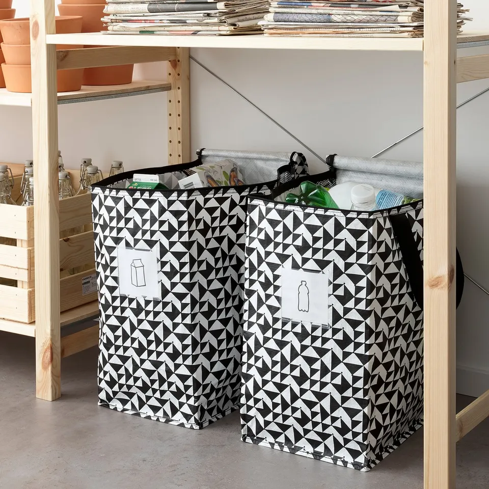 Black and white triangular patterned KNALLA bag fits under shelves, holds various recyclables.