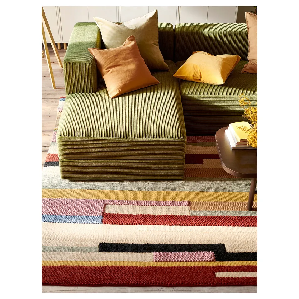 Modern living room with green JÄTTEBO modular sofa, yellow pillows, and colourful striped rug.