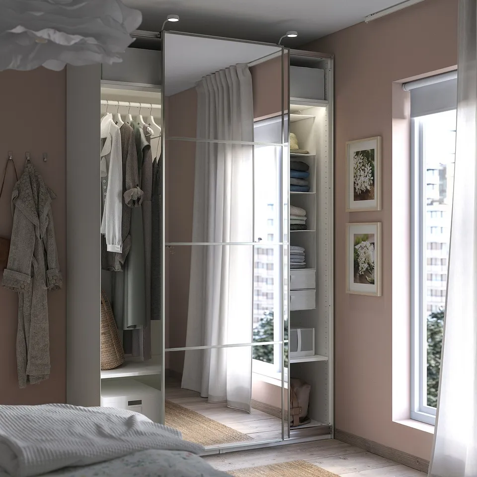 Modern bedroom with PAX wardrobe, mirrored doors, hanging clothes, shelves, and grey curtains.