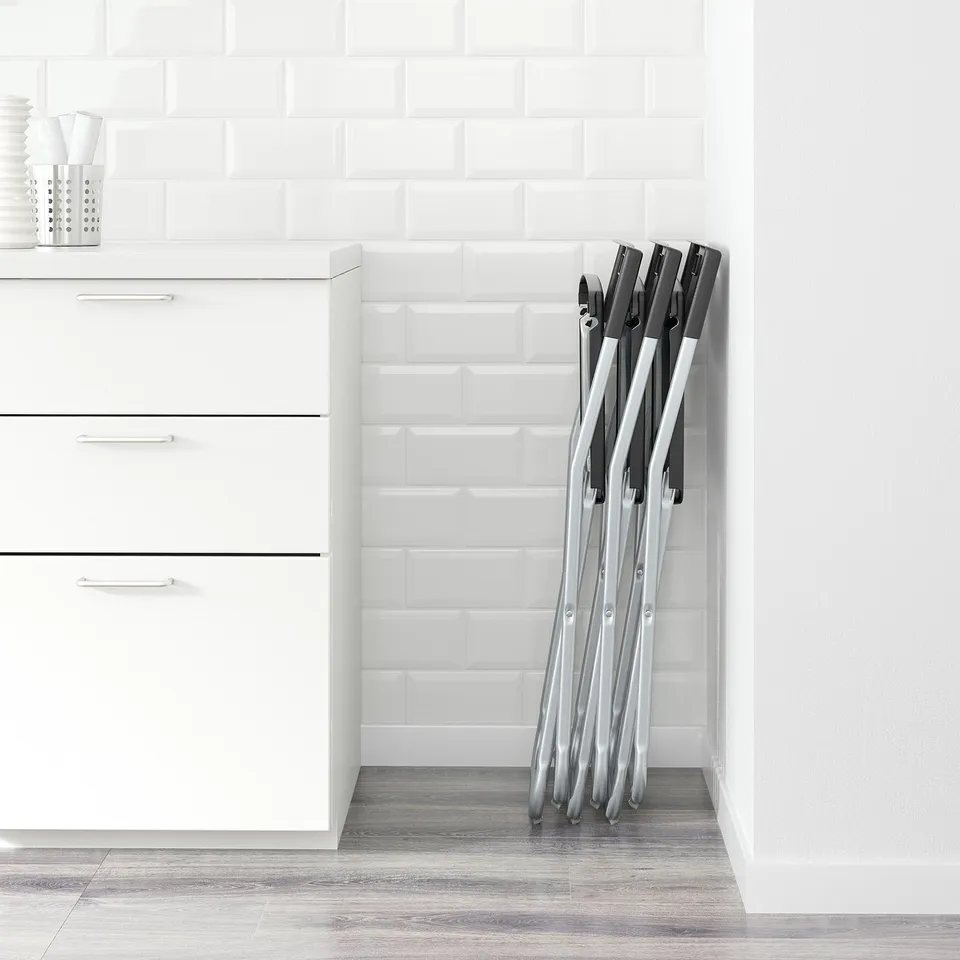Stacked foldable chairs against a tiled wall next to a white cabinet with drawers.