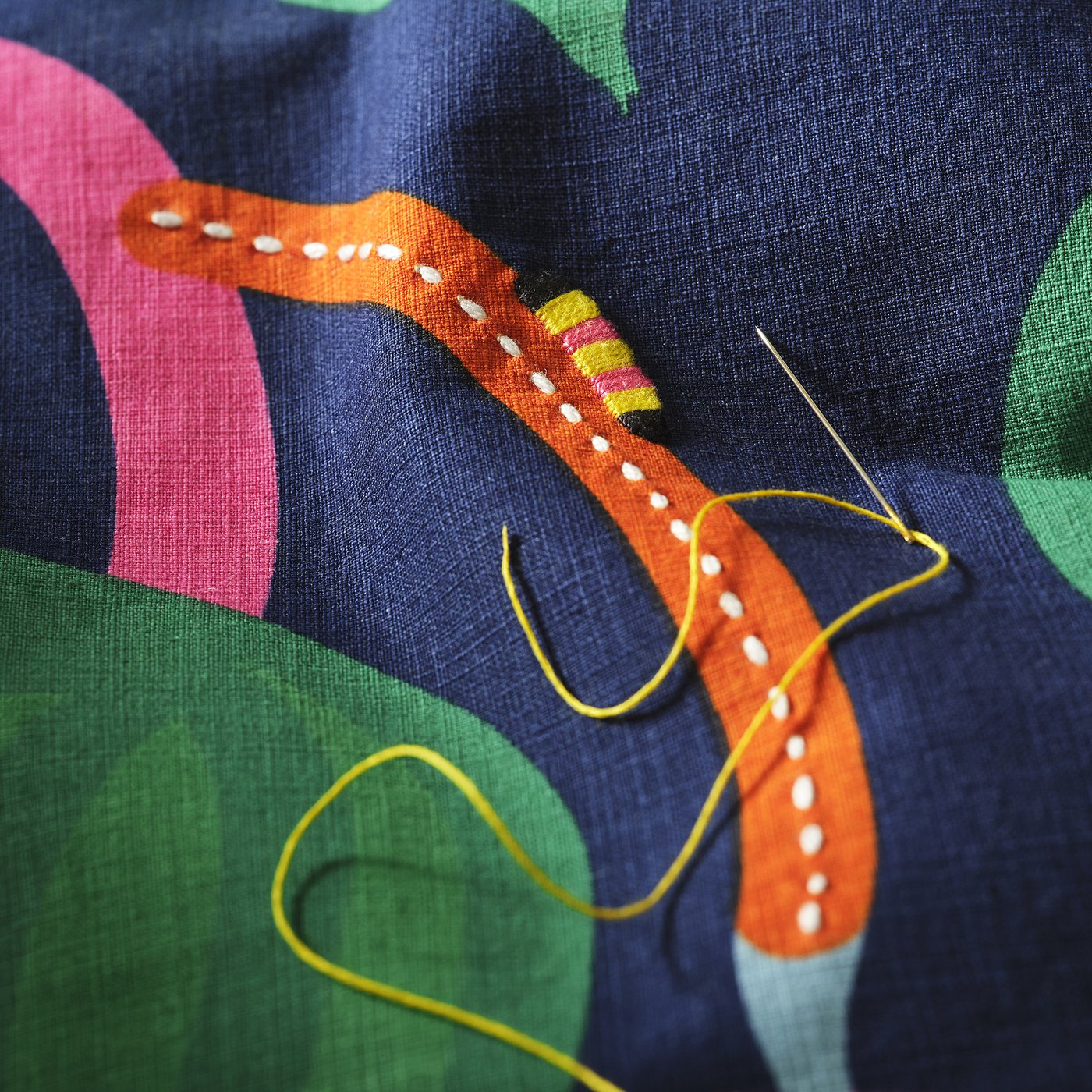 Close-up of hand-embroidered cushion cover showcasing vibrant caterpillar and stitching on abstract fabric.