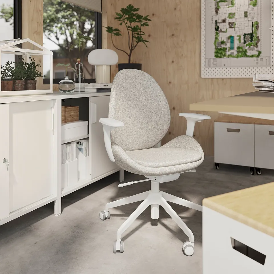 Ergonomic white office chair with adjustable armrests, backrest, and lumbar support on wheels beside a wooden desk with decor items.