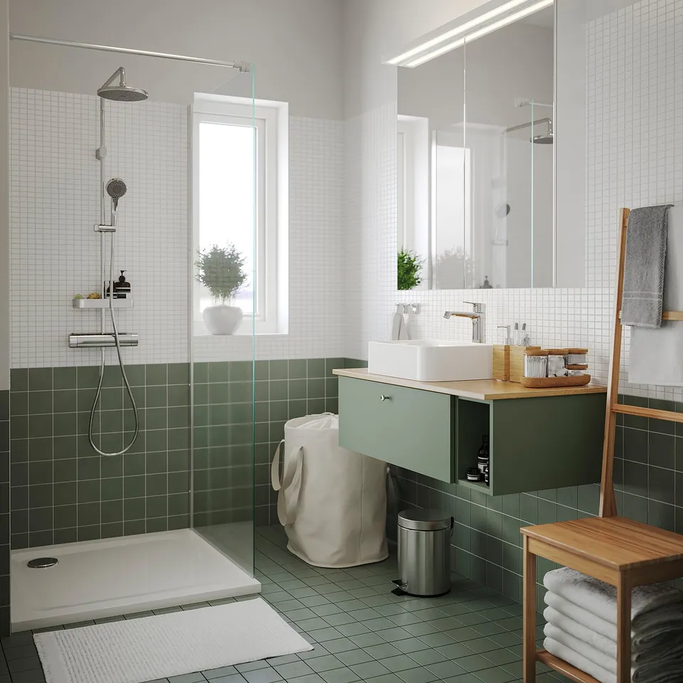 Modern bathroom with green tiled walls, white fixtures, glass shower screen, wooden accents, and potted plant.