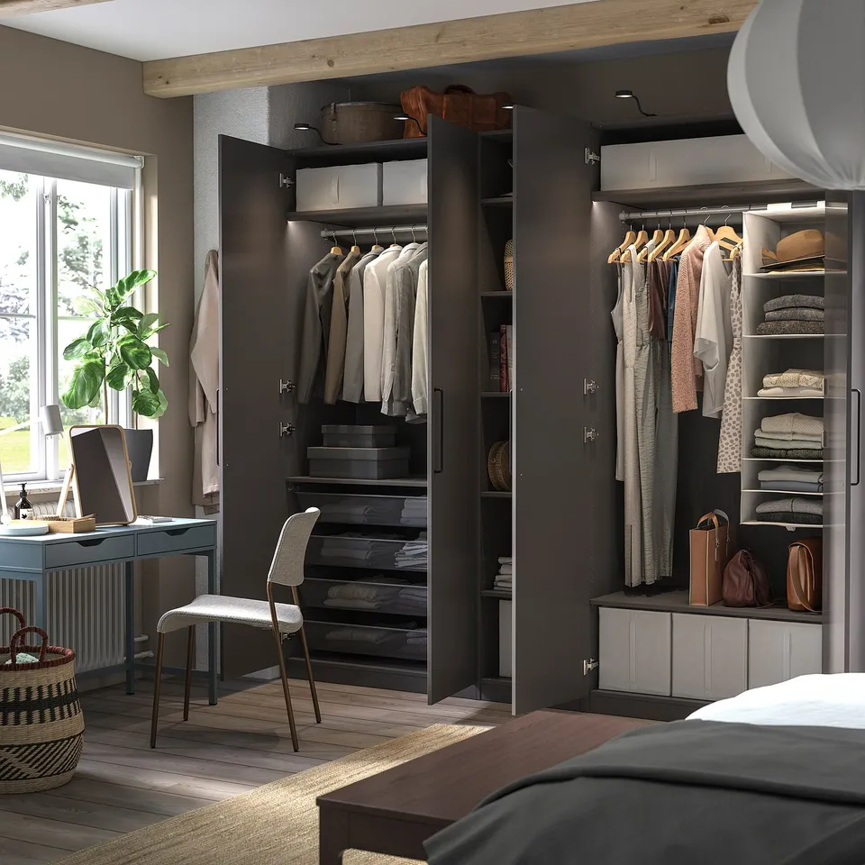Modern bedroom with black PAX wardrobes, shelves with clothes, and a light blue desk near a large window with a plant.