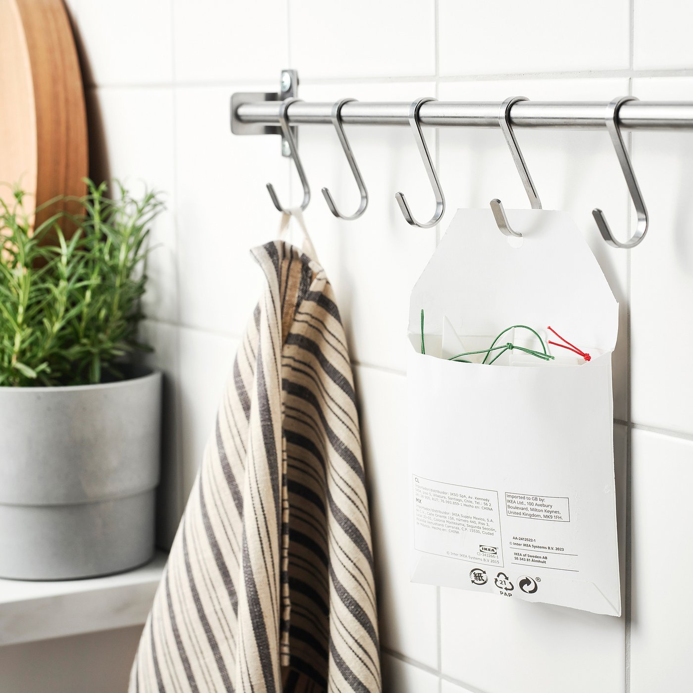 Striped towel and labelled bags hang from chrome s-hooks on a shower curtain bar, showing FÖNSTERFIKUS reusable labels.