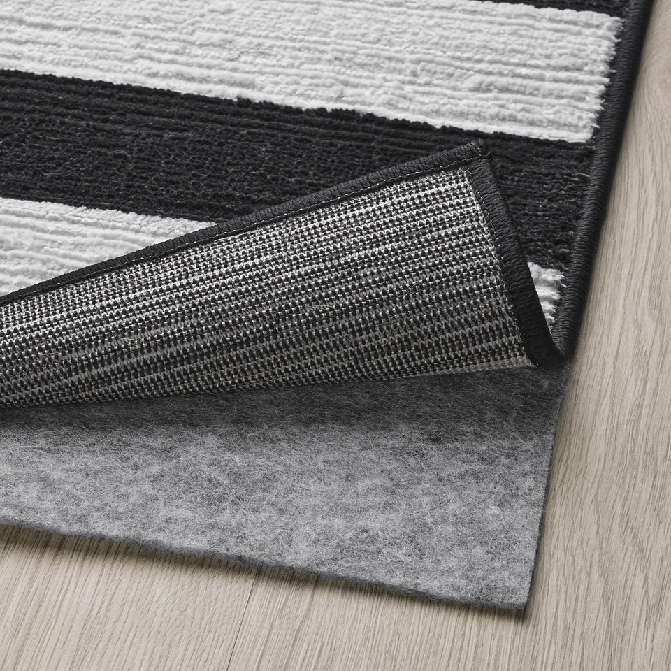 Black and white striped rug with a textured pattern, featuring a non-slip rubber base for safety.