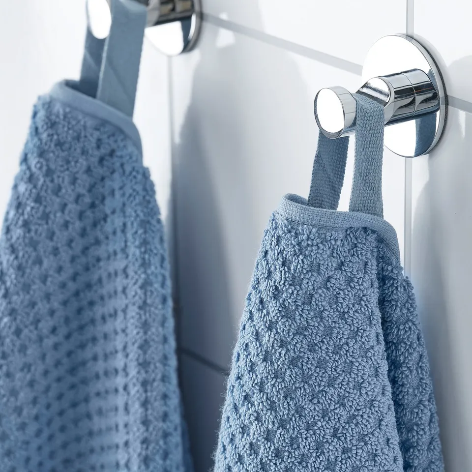 Two light blue towels hang on chrome hooks, showcasing their soft, fluffy texture and absorbent cotton material.
