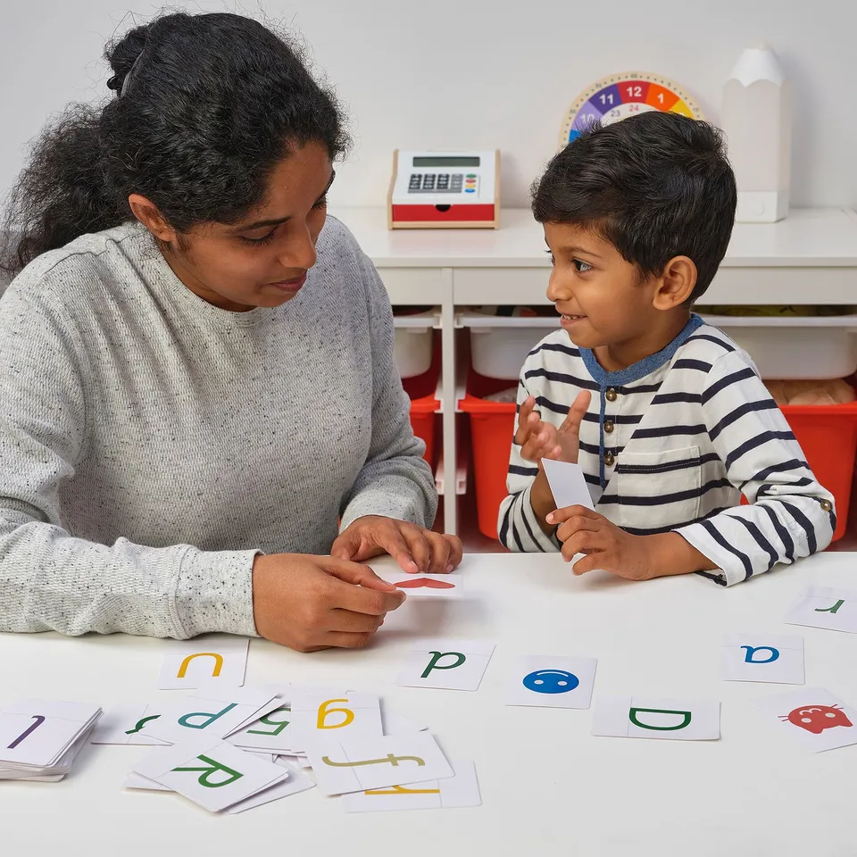 Person & boy with letter cards, learning in classroom.