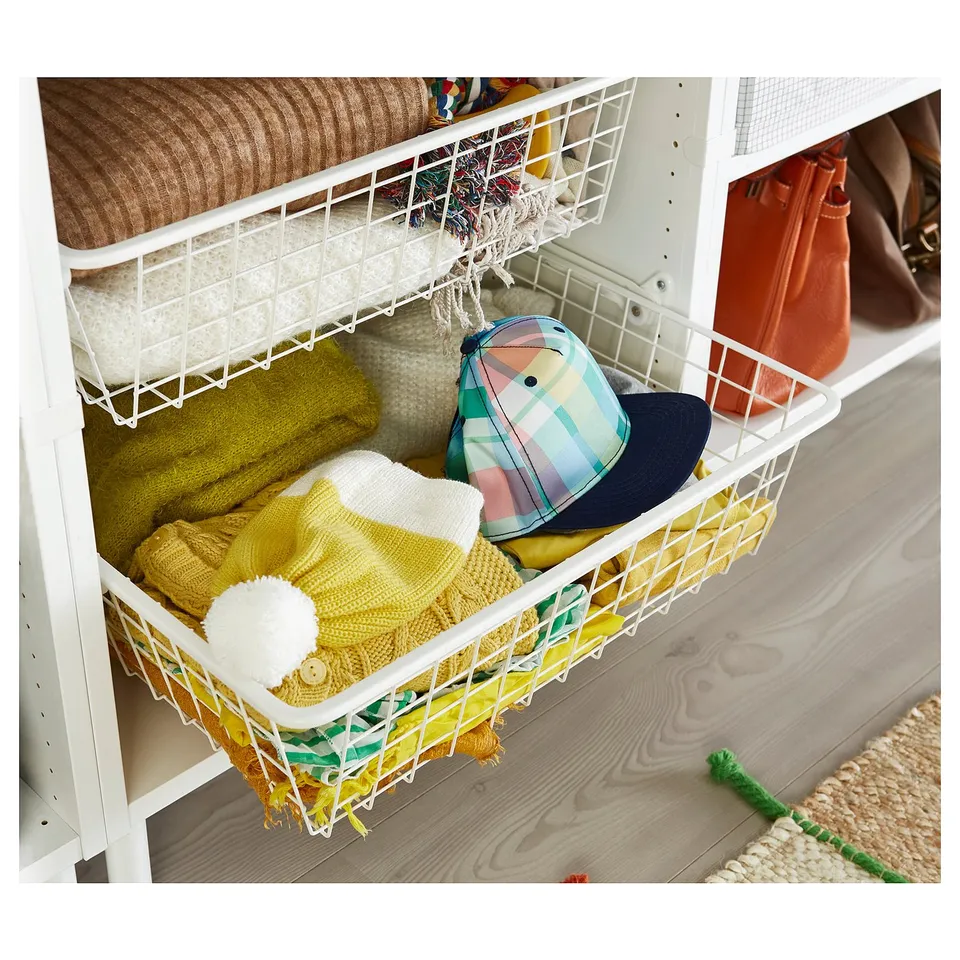 White metal mesh storage baskets hold colourful blankets and a hat on a shelf.