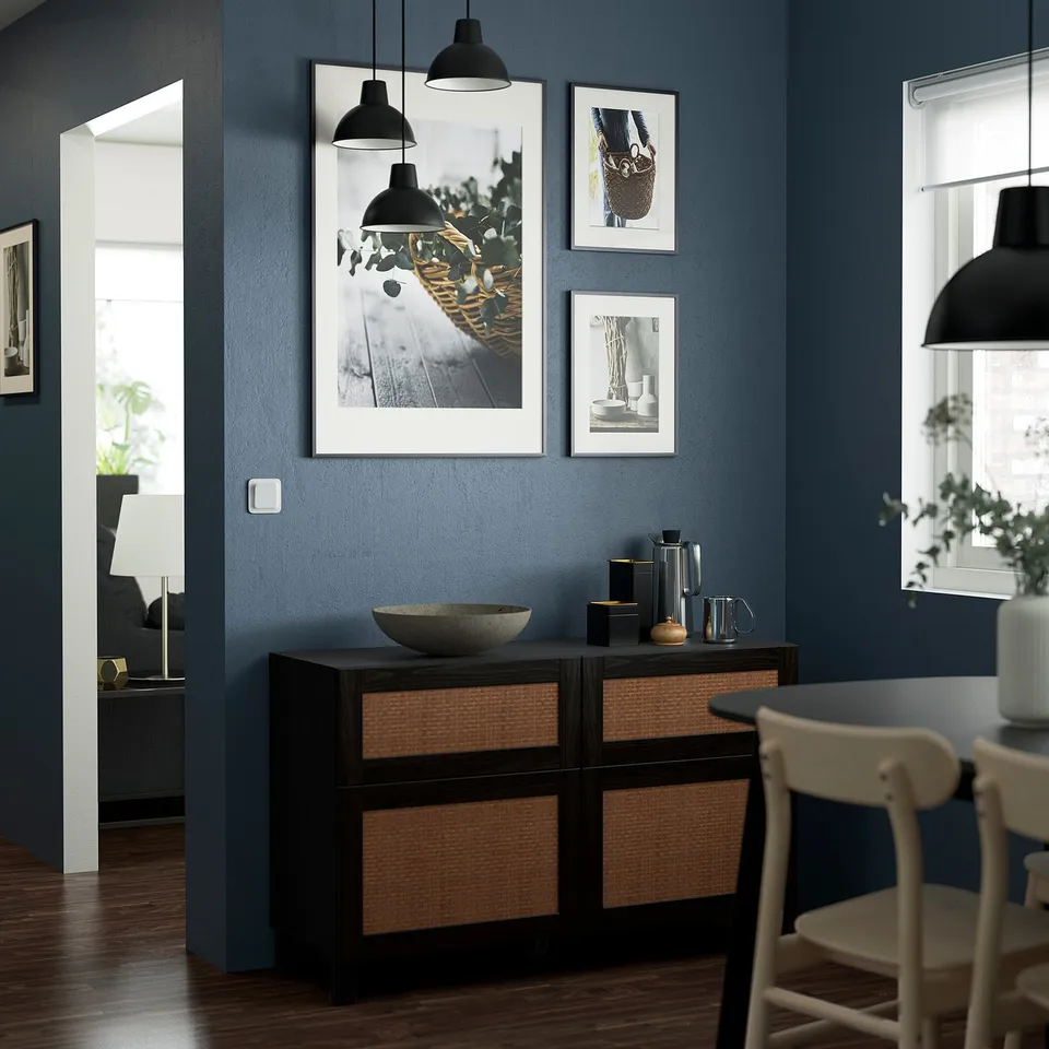 Modern dining room with dark blue walls, BESTÅ sideboard, bowl, glassware, framed pictures, and pendant lights.