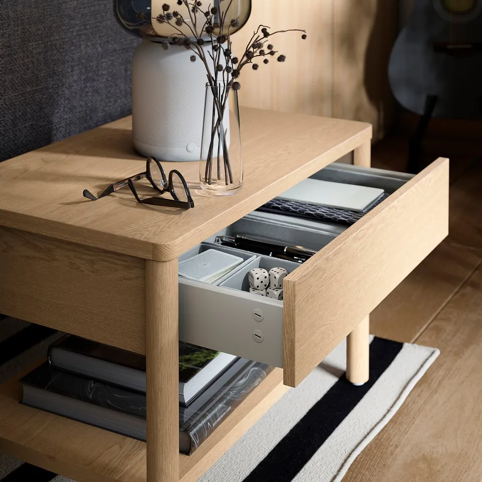 Wooden side table with open storage shelf and soft-close drawer, holding books and dice, with decorative items on top.