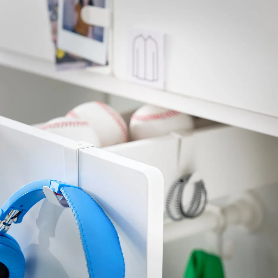 Blue kids headphones hang on a white organiser shelf, with sports balls stored above.