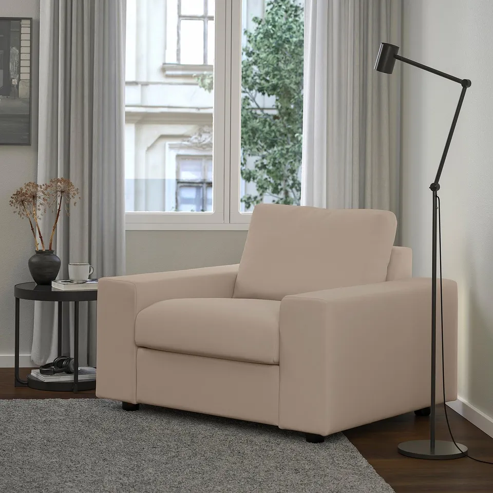 Beige VIMLE armchair between crate table and tall lamp, with a large window, stylish decor, and inviting ambiance.