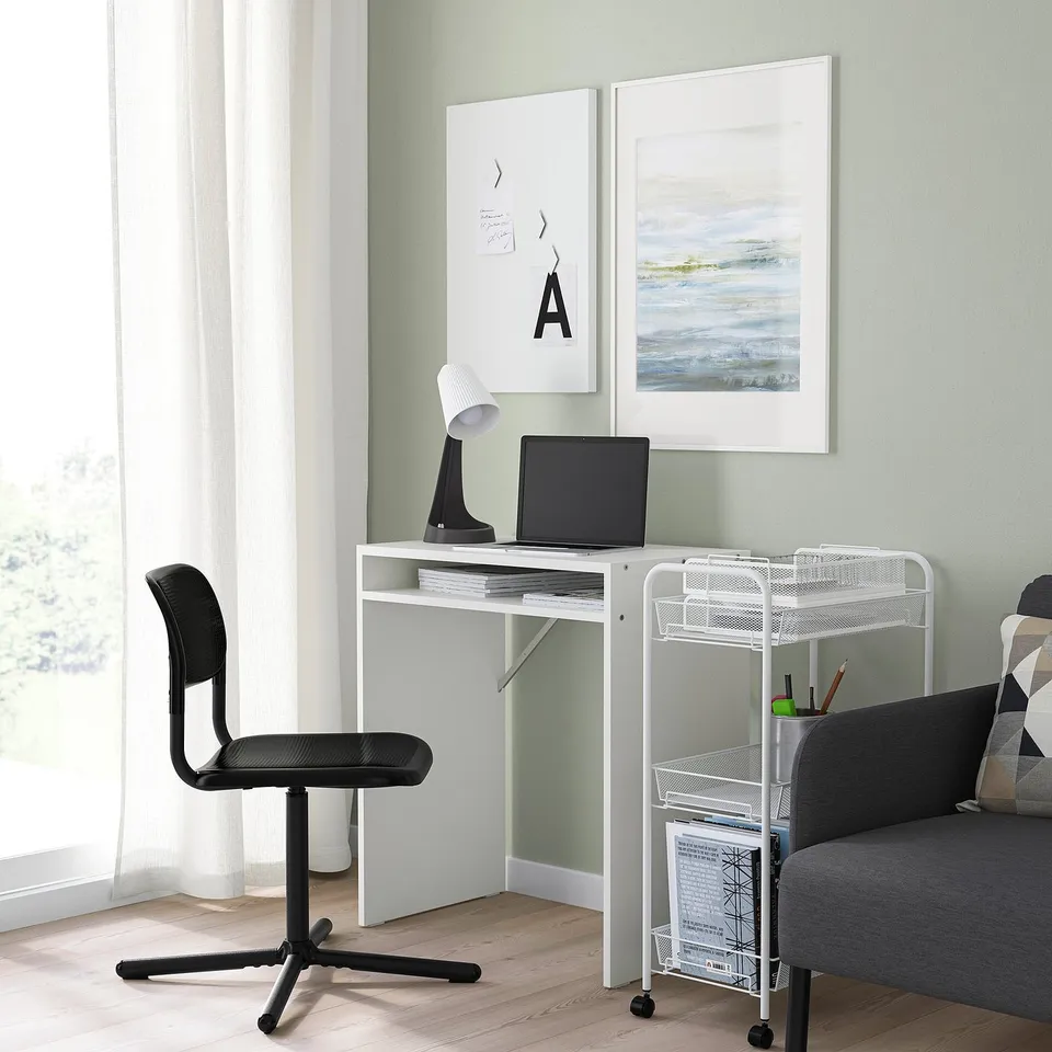 Small white desk with laptop, black swivel chair, grey couch, art prints.