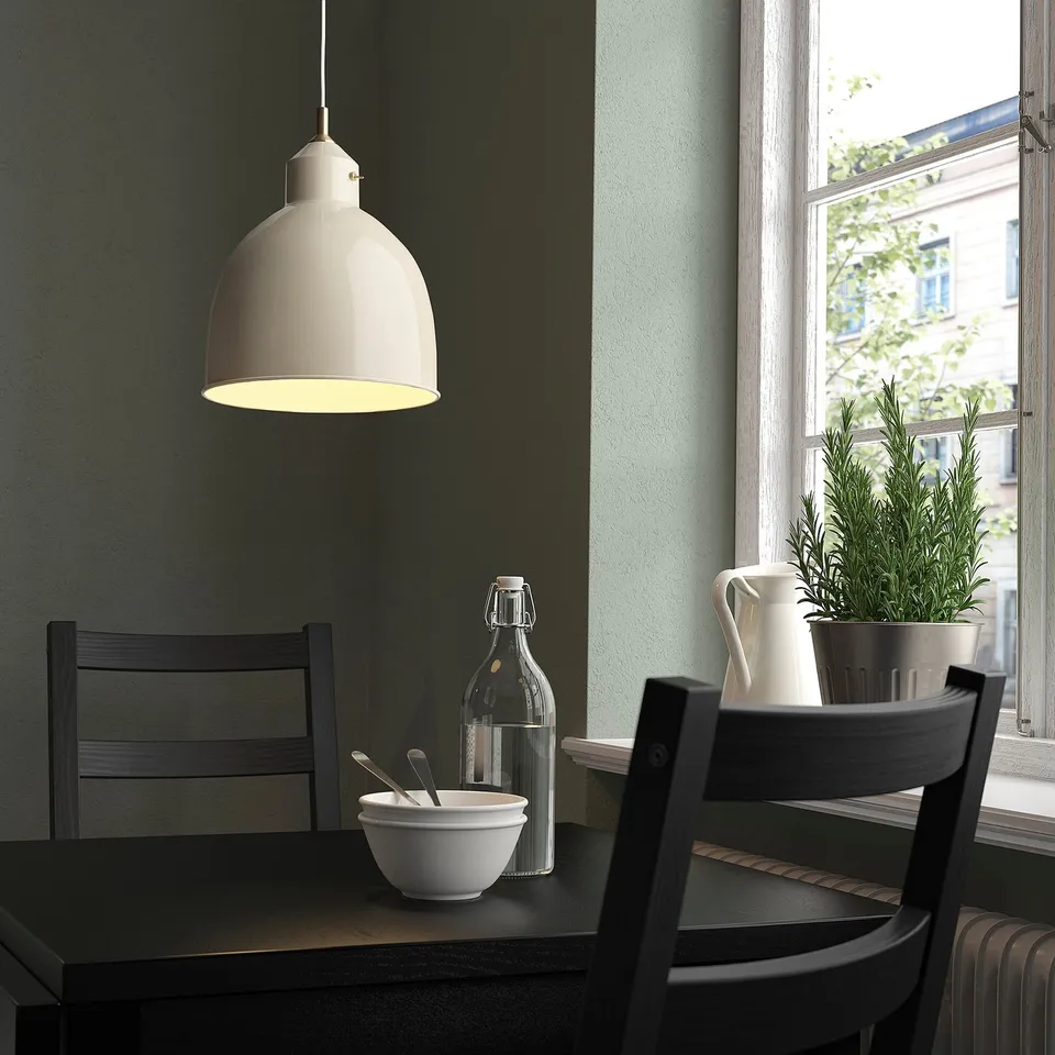 Small white RÖDFLIK lamp hangs near a window, illuminating a dark table with chairs and decor.