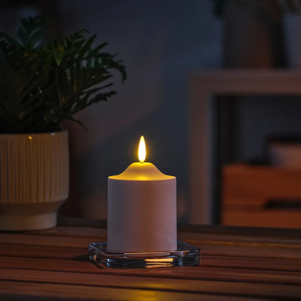 White SMÅLOM led candle on glass coaster, small, near a potted plant.