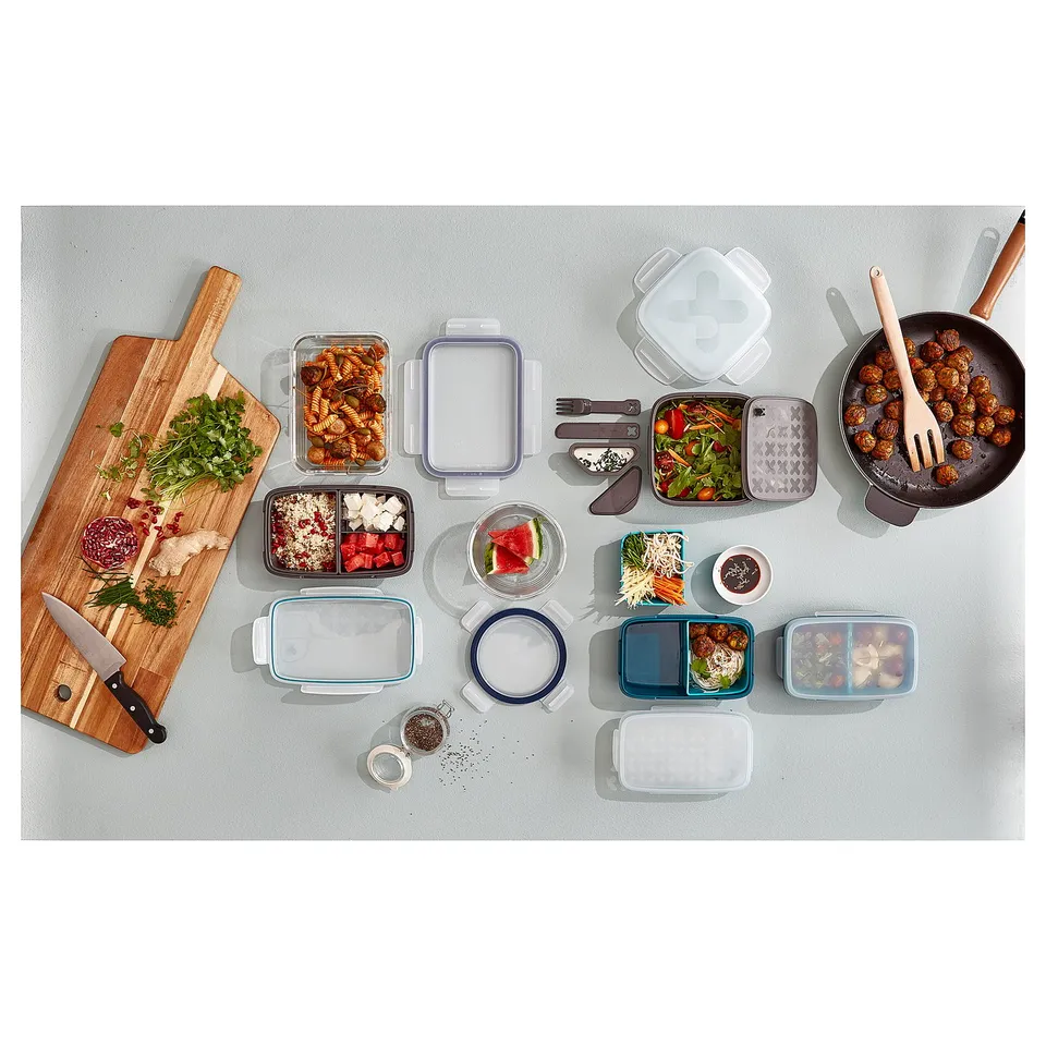 Variety of food containers with different colours, shapes, and contents, plus a wooden chopping board and knife.