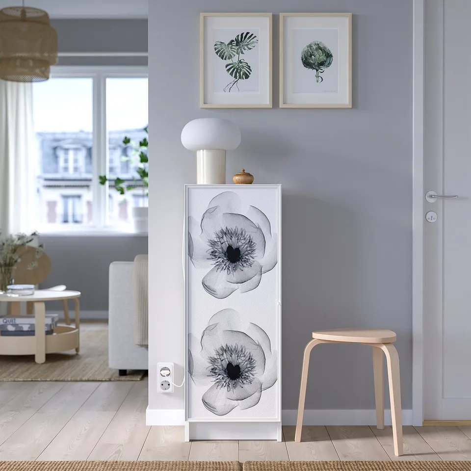 Stylish white BILLY bookcase with floral door, lamp, prints, stool, grey wall, cosy living area.