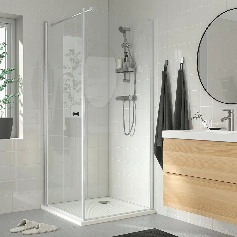Modern bathroom with white-tiled shower, chrome fixtures, wooden vanity, and green plants.