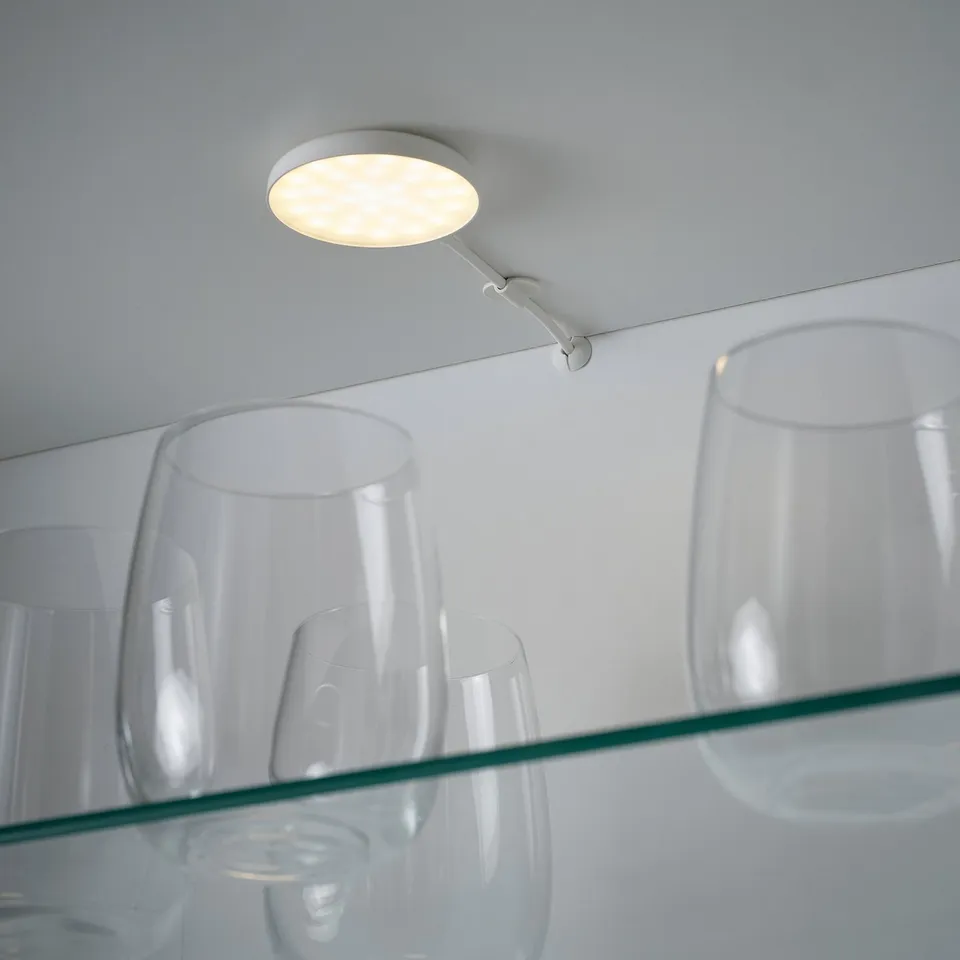 Clear glasses on glass shelf, lit by round ceiling spotlight.