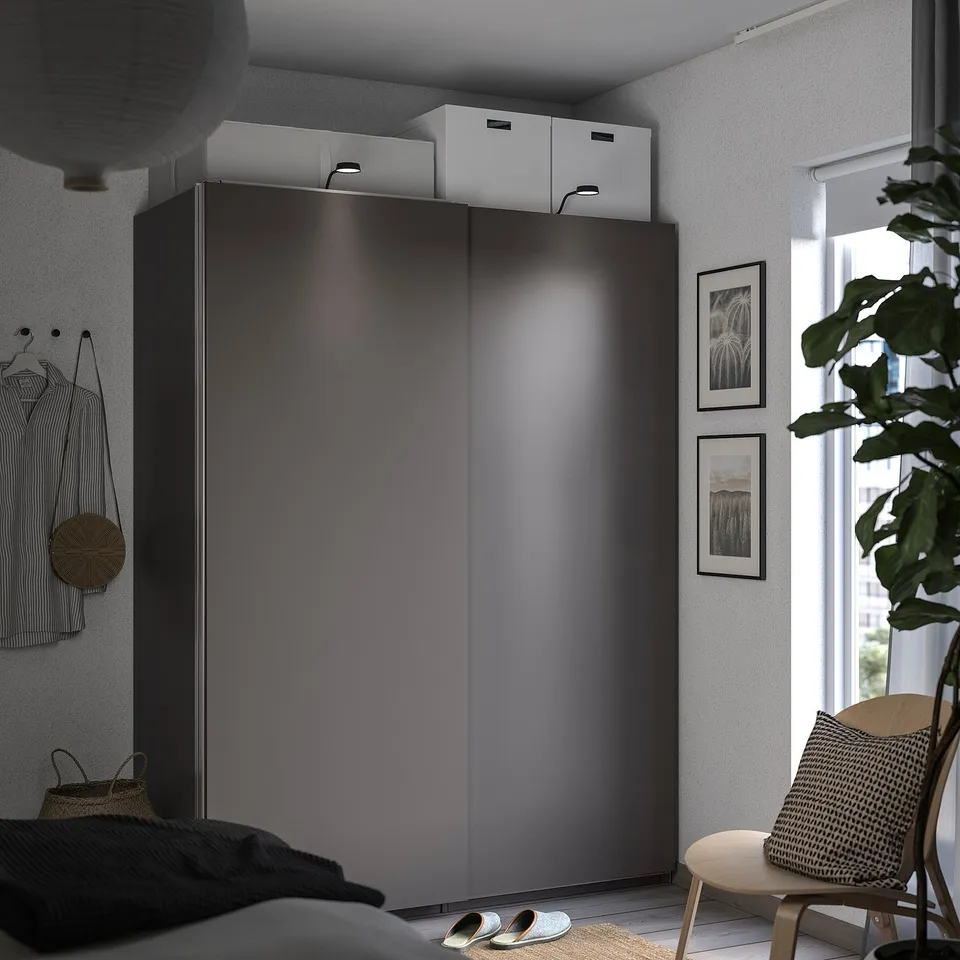 Grey wardrobe, plant, pictures, shirt, bag, chair in cosy bedroom.