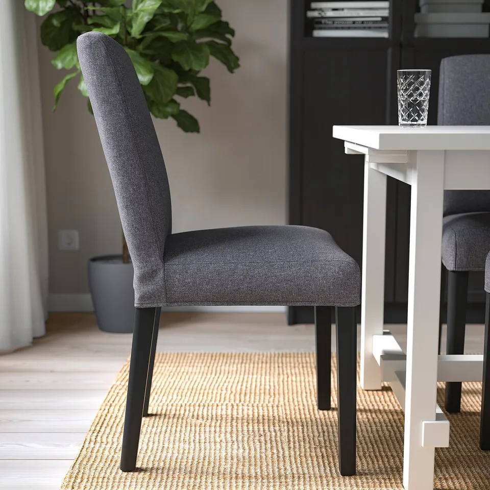 Chair with dark grey fabric and black wooden legs near a white table. Seat and backrest padded for comfort.