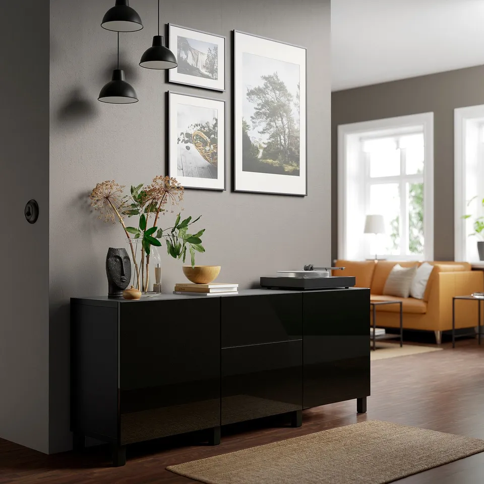 Black BESTÅ sideboard with 2 drawers, flowers, bowl & books. Near orange sofa & rug, beside a window.