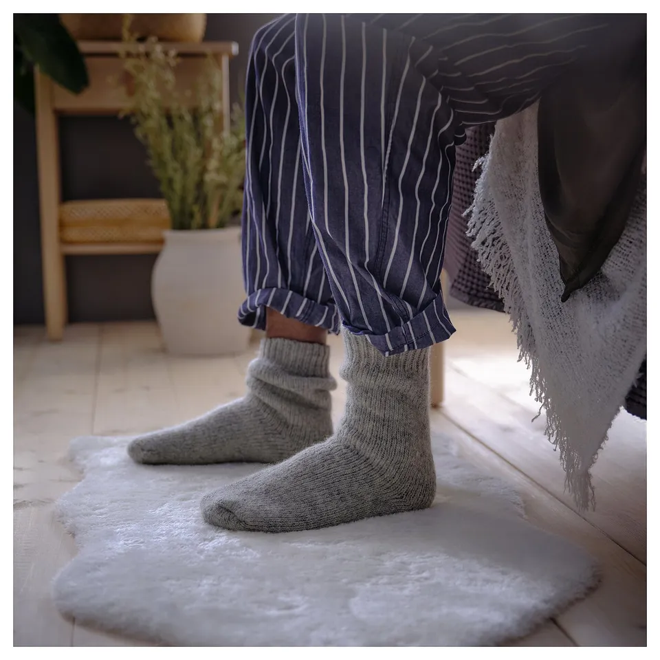 Person wearing TOFTLUND light blue striped pants and grey knitted socks stands on white furry rug.