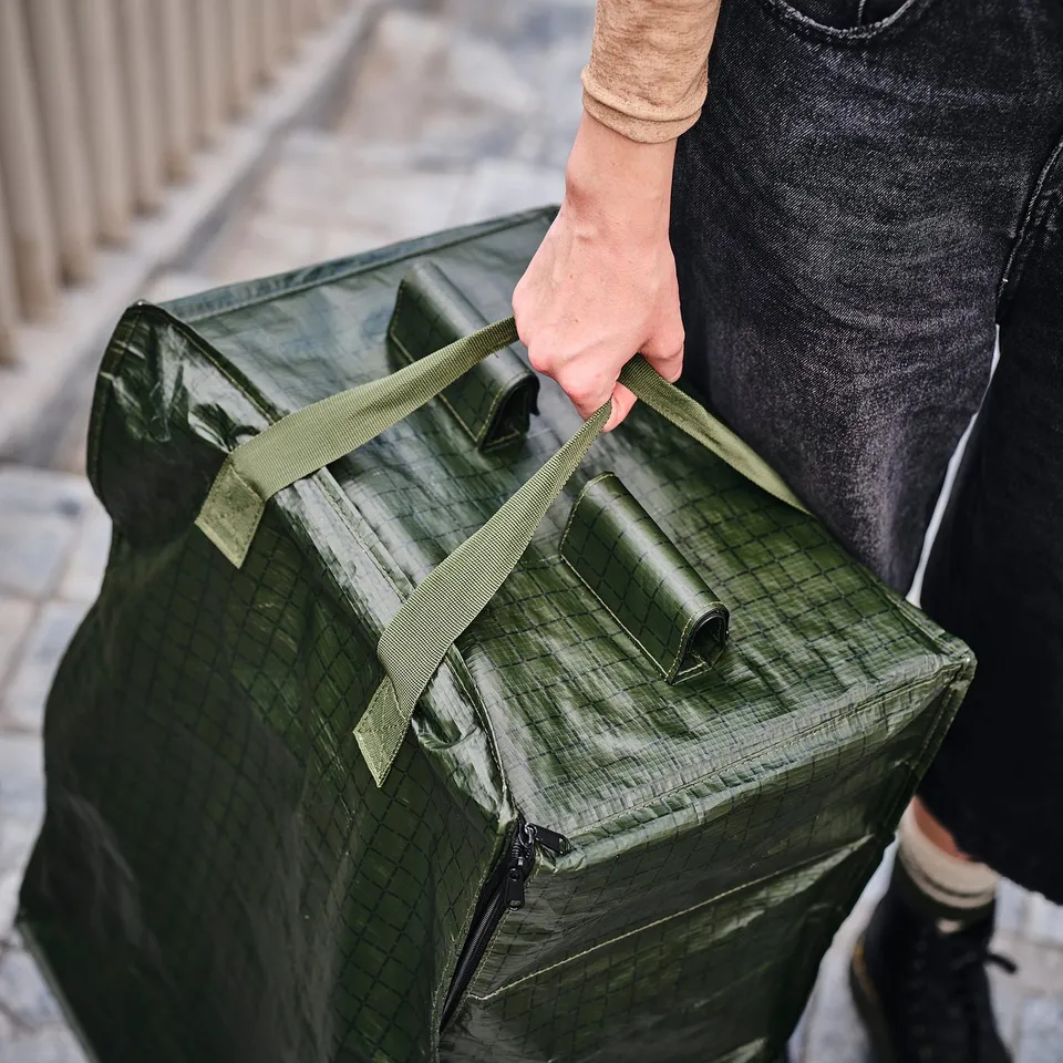 A person holding a green KOMPISHÄNG storage bag with carrying straps.