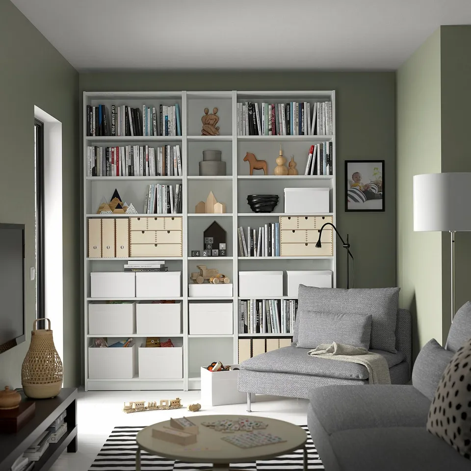 Modern living room with BILLY white bookshelf displaying books and toys, grey sofa, and striped rug.