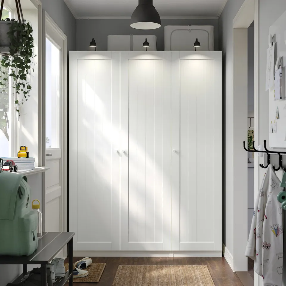 Modern white PAX wardrobe with lit top shelf and backpack beside it.