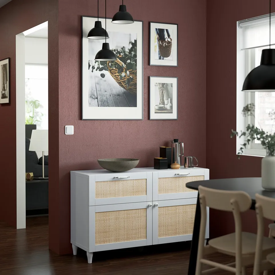White BESTÅ sideboard with rattan, decor, & lights complements maroon wall.