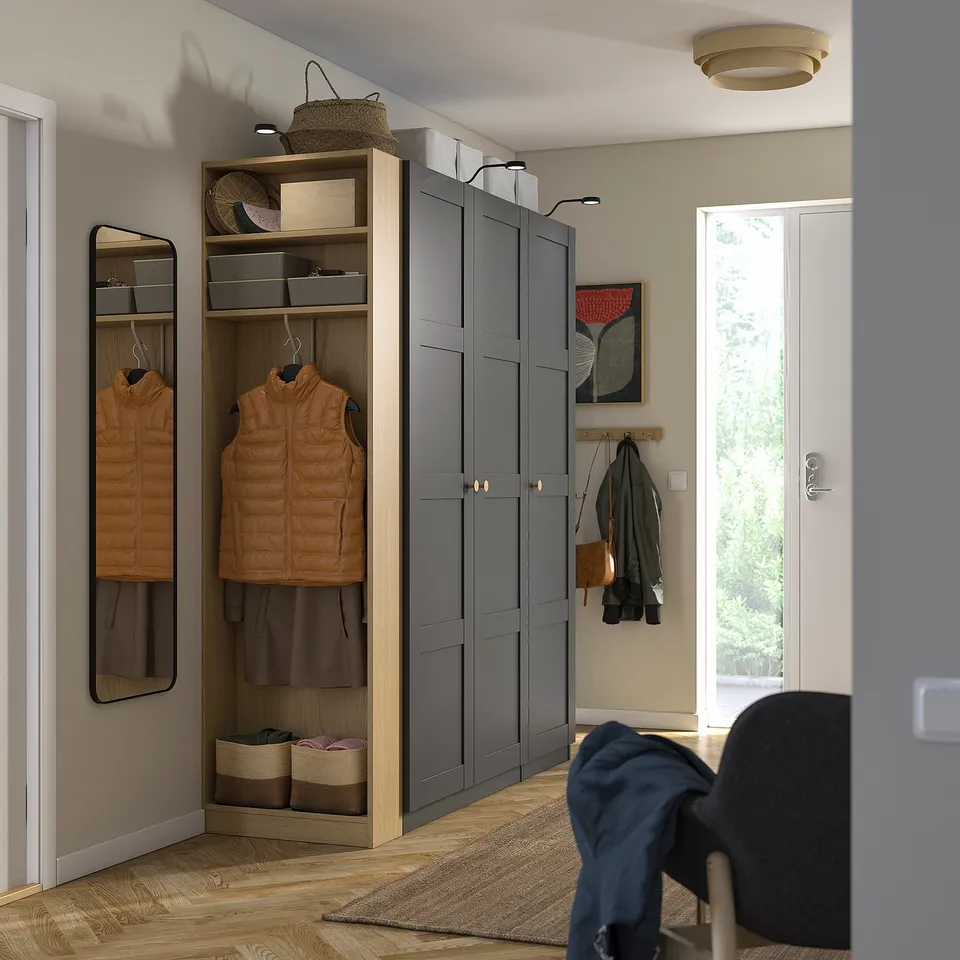 Modern grey wardrobe with shelves and hanging space in hallway, near mirror and brown leather vest.