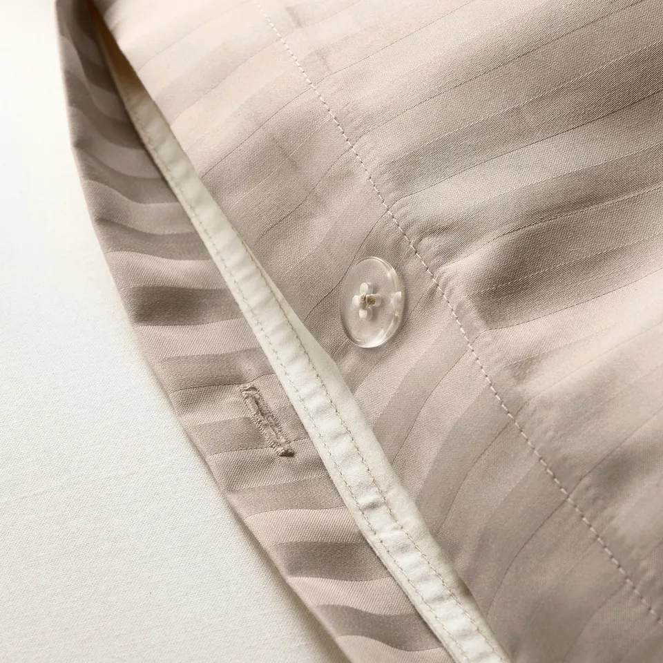 Close-up of duvet cover set with subtle stripes and moisture-wicking fabric, featuring button.