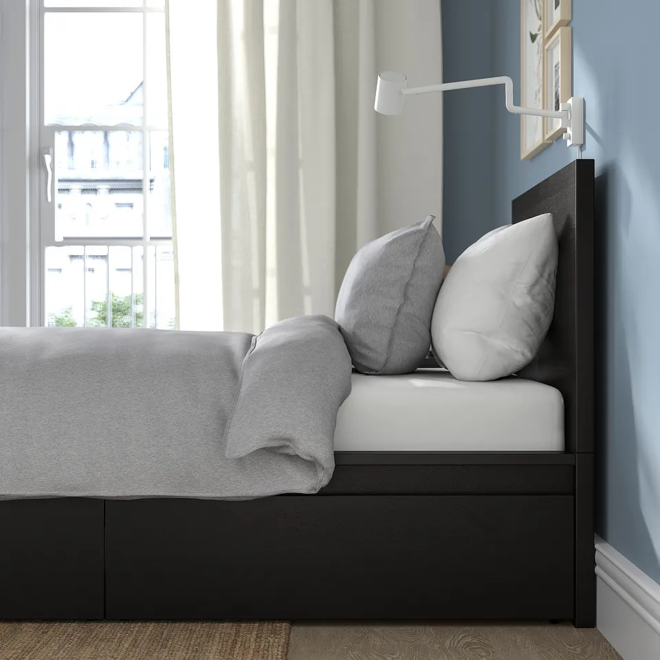 Bed frame with storage drawers, adjustable sides, white pillows, grey blanket, light curtains.