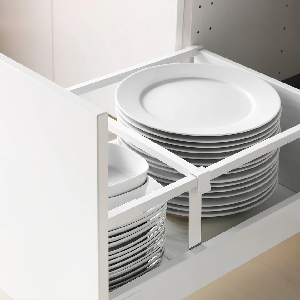 White kitchen cabinet with open drawer, neatly storing stacks of white plates and bowls. Drawers have a self-closing mechanism.