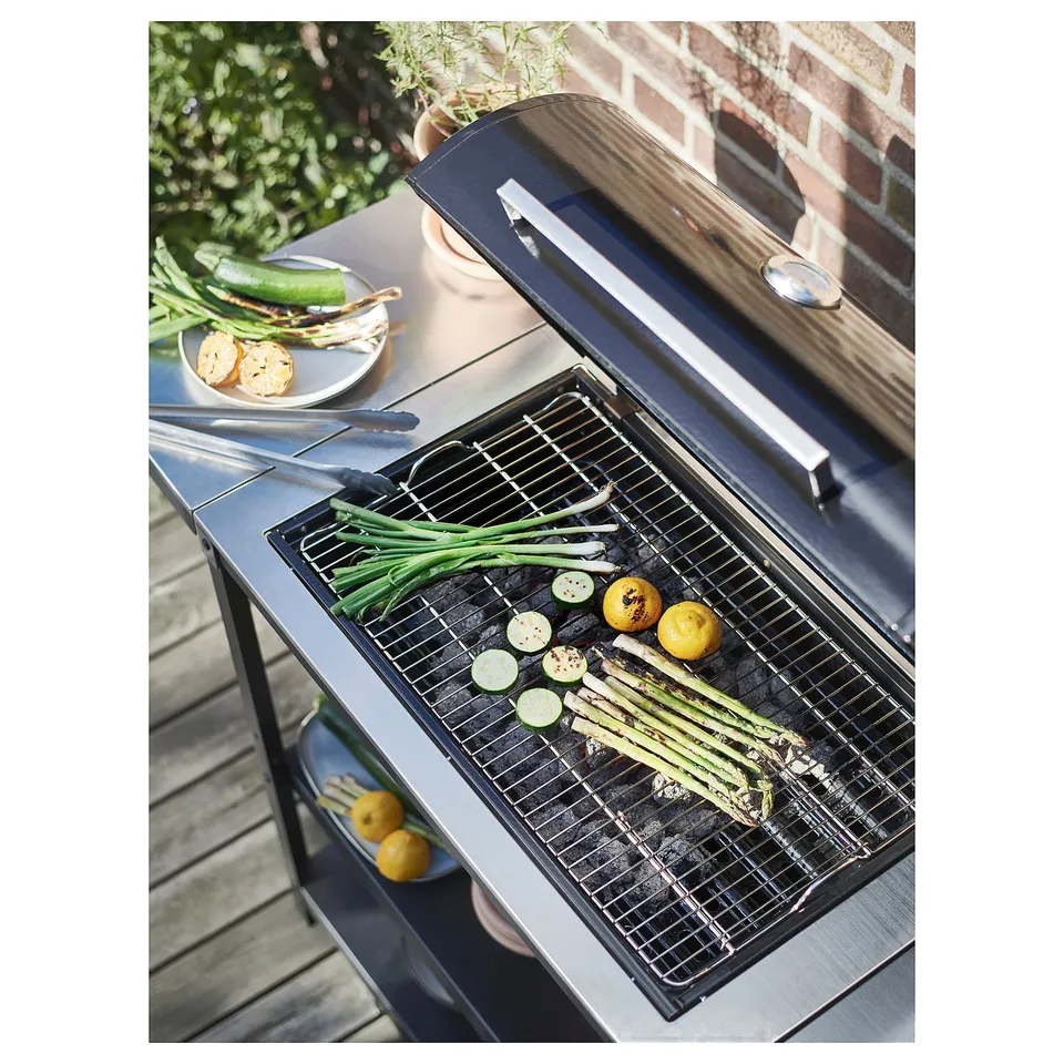 Black GRILLSKÄR charcoal grill grilling vegetables; stainless & steel, outdoor setting.